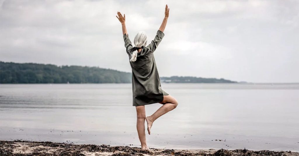 middle aged woman balancing on one leg at the beach